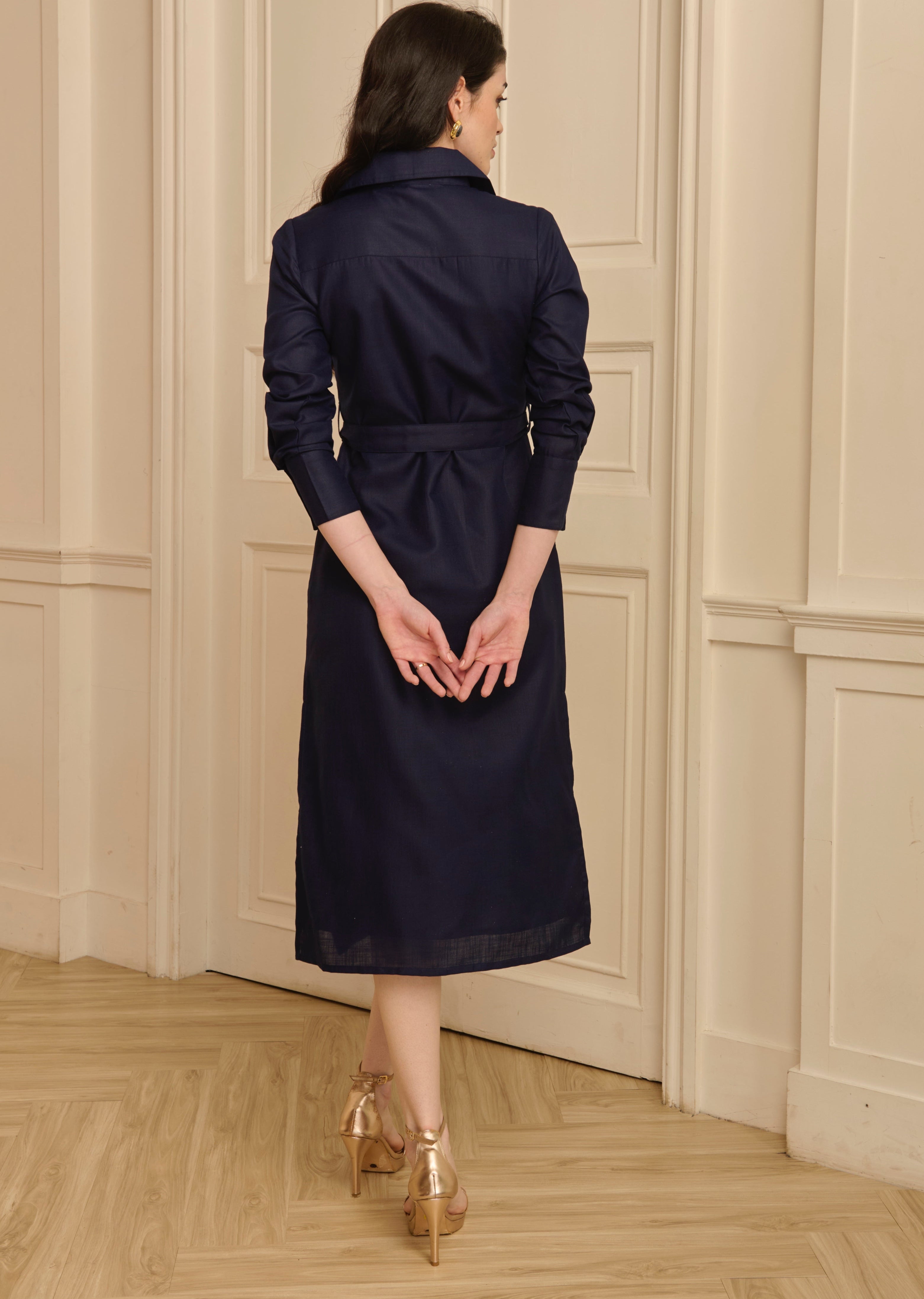 Woman in a navy coat standing in a room with wooden flooring and paneled walls.